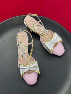 Pink high heels with silver bows on a black plate against a red background