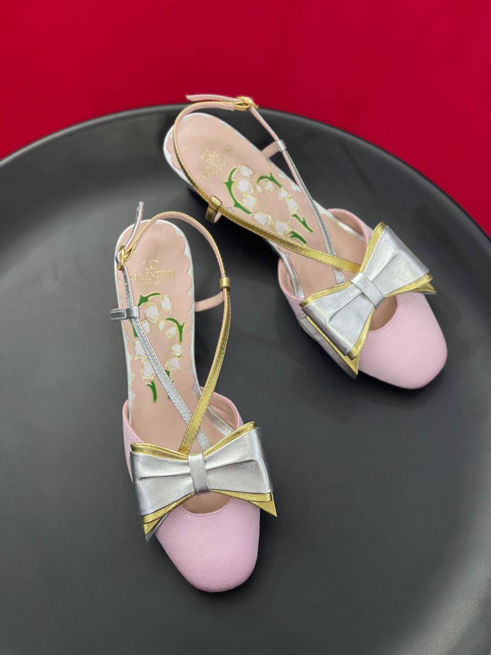 Pink high heels with silver bows on a black plate against a red background